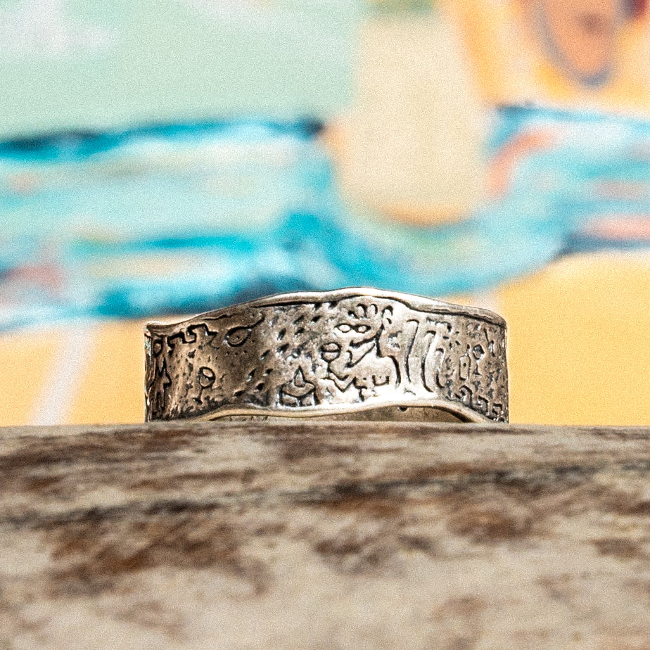 A silver ring against a colourful backdrop. Engraved with mediterranean imagery including adonis and a dog.
