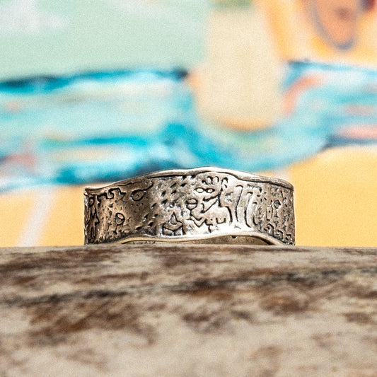A silver ring against a colourful backdrop. Engraved with mediterranean imagery including adonis and a dog.