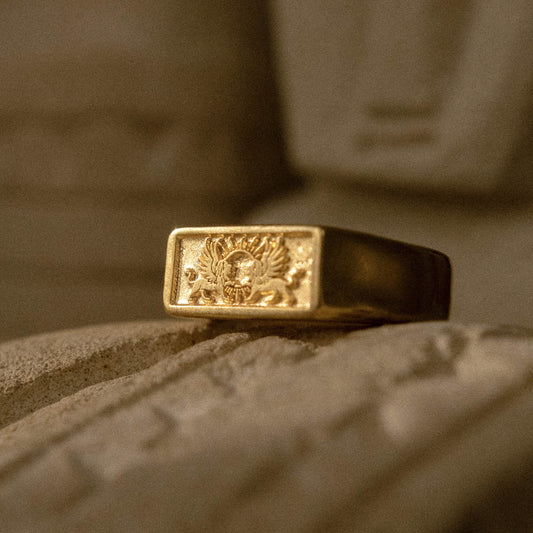 Product shot of the gold Gift of Gods ring on a textured stone surface.