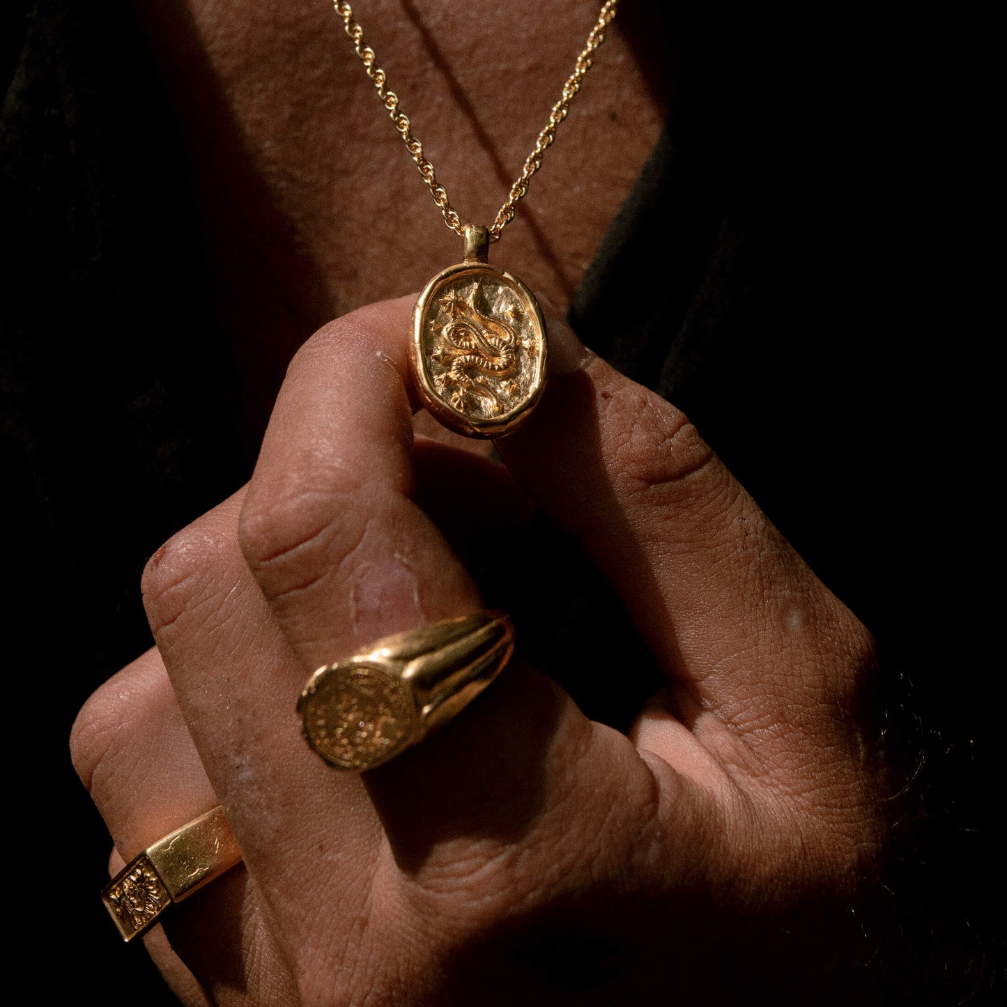 An image showing the gold Dreamer pendant being worn by a man with the gold True North ring and the gold Gift of Gods ring on his hand.